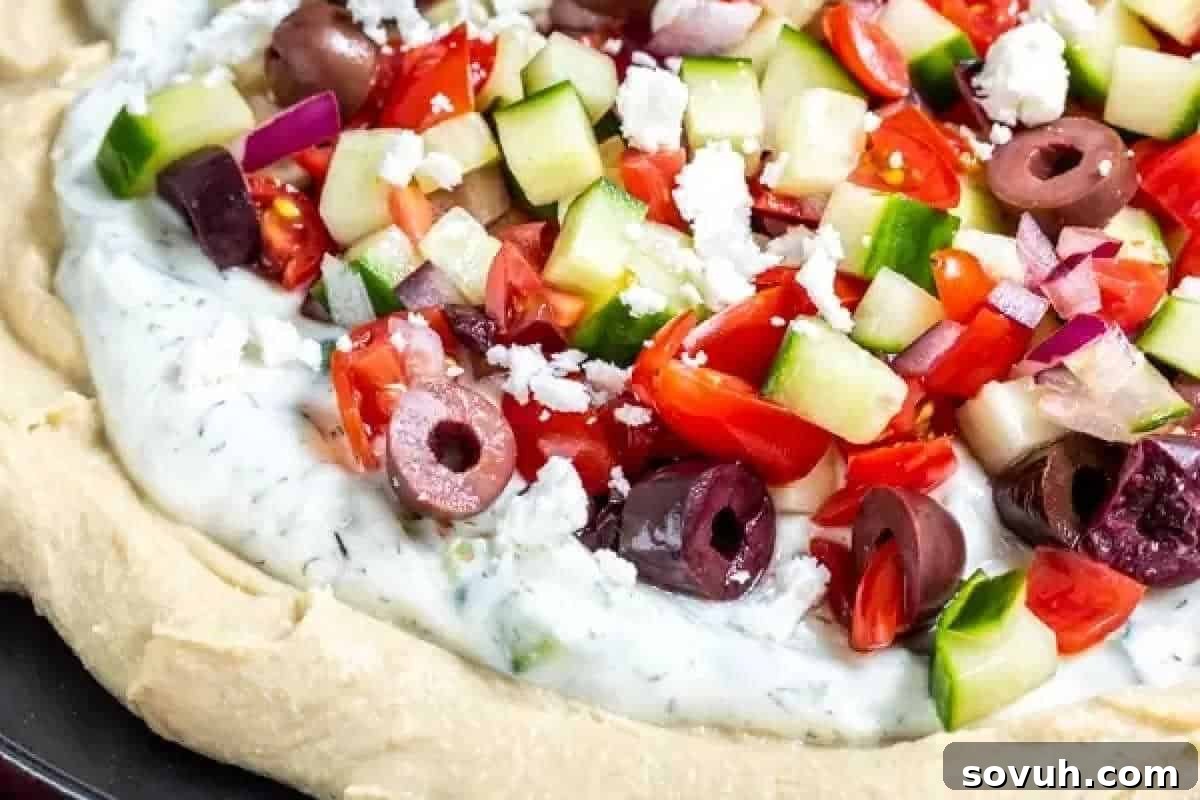 Fresh vegetable toppings on a creamy layered dip with cucumbers, tomatoes, red onion, olives, and feta cheese.