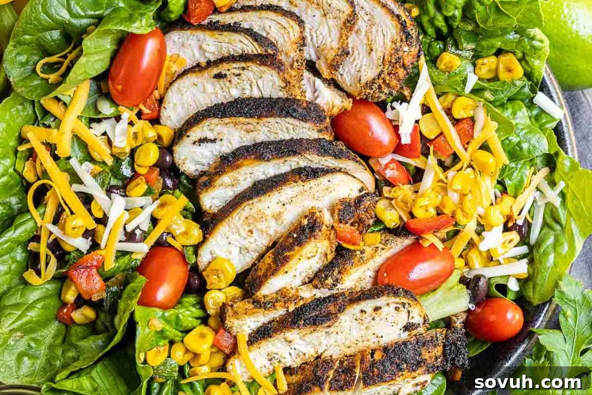 Grilled chicken slices on a bed of lettuce with cherry tomatoes, corn, shredded cheese, and peppers.