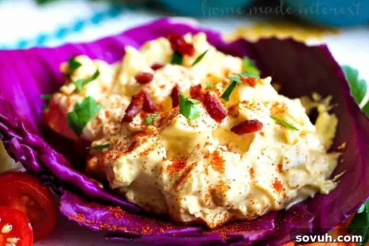 Egg salad garnished with paprika and chopped herbs, served in a purple cabbage leaf, alongside sliced cherry tomatoes.