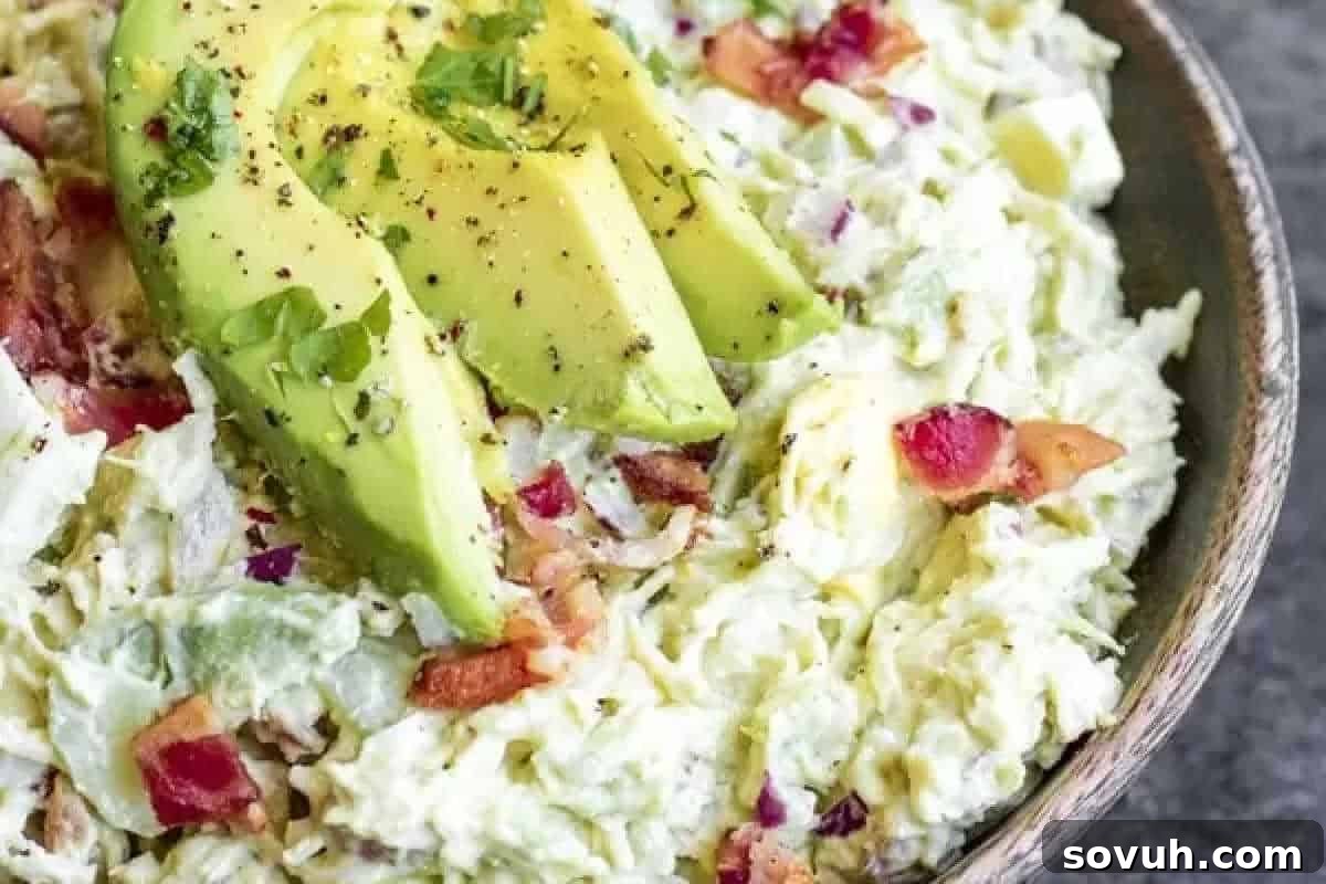 A bowl of chicken salad topped with sliced avocado, tomatoes, and herbs.
