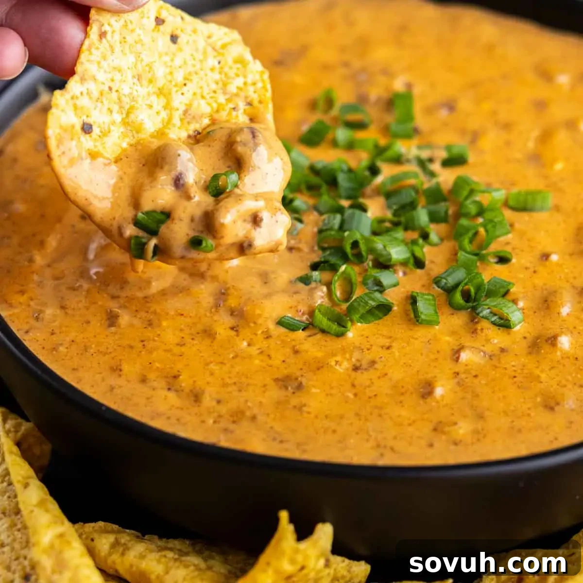 A tortilla chip generously coated in a rich, creamy chili cheese dip, garnished with chopped green onions.