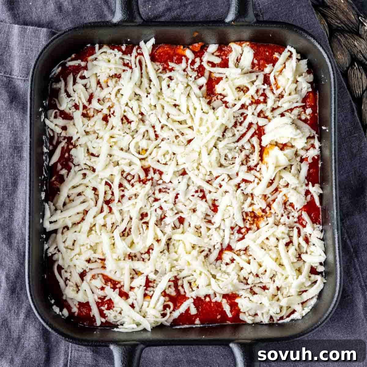 A baking dish with a creamy cheese layer, topped with marinara sauce and a sprinkling of shredded mozzarella cheese.