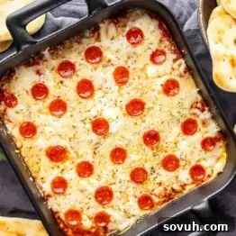 A square pizza dip topped with pepperoni and cheese in a black baking dish, ready to serve.
