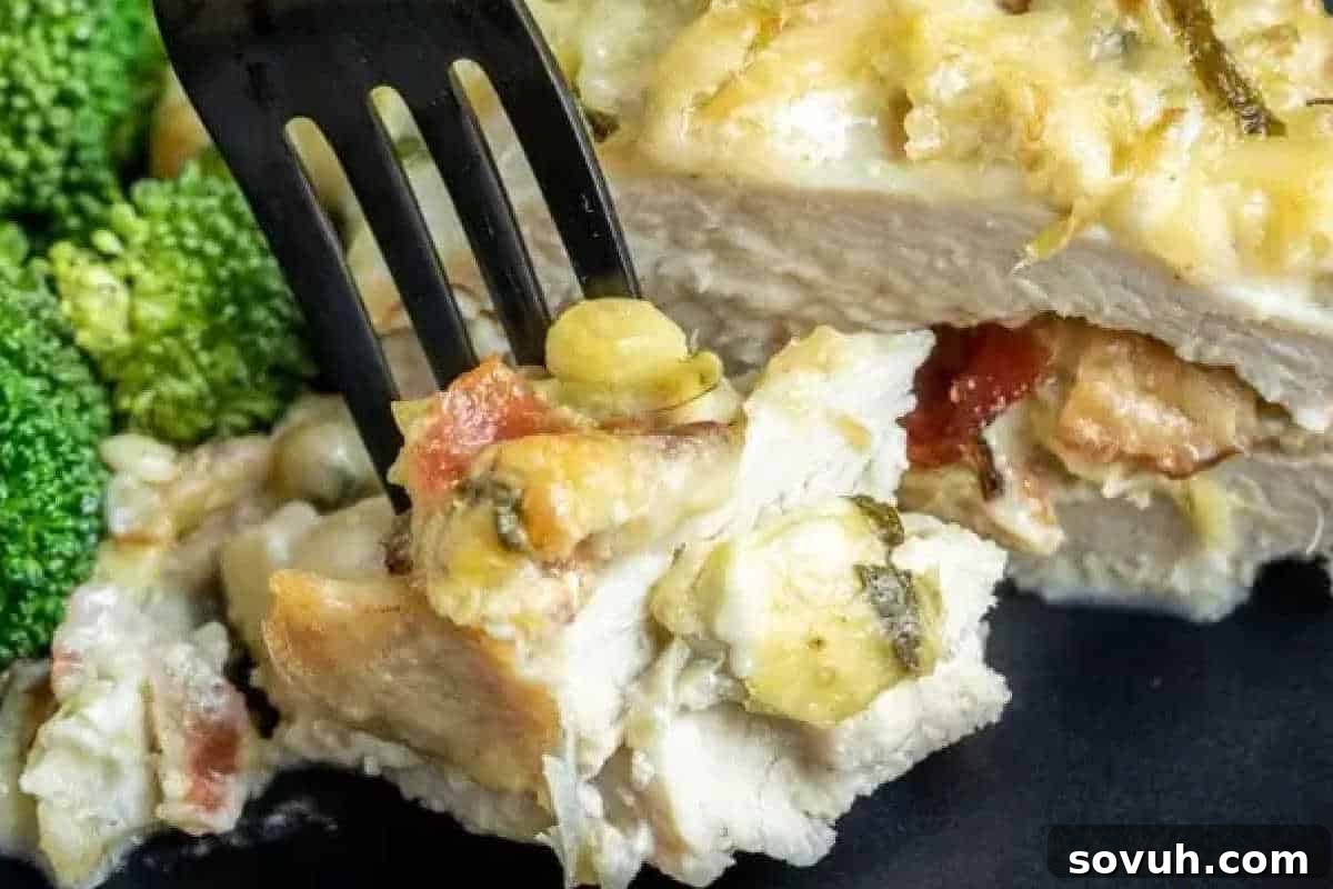 A fork lifts a generous piece of cheesy chicken casserole, brimming with vegetables, from a plate, highlighting its rich, bubbly texture.