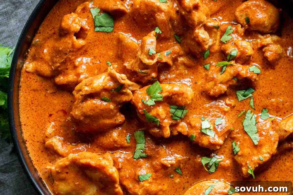 A close-up of a rich, orange-hued curry filling a bowl, featuring tender pieces of meat and garnished with finely chopped cilantro.