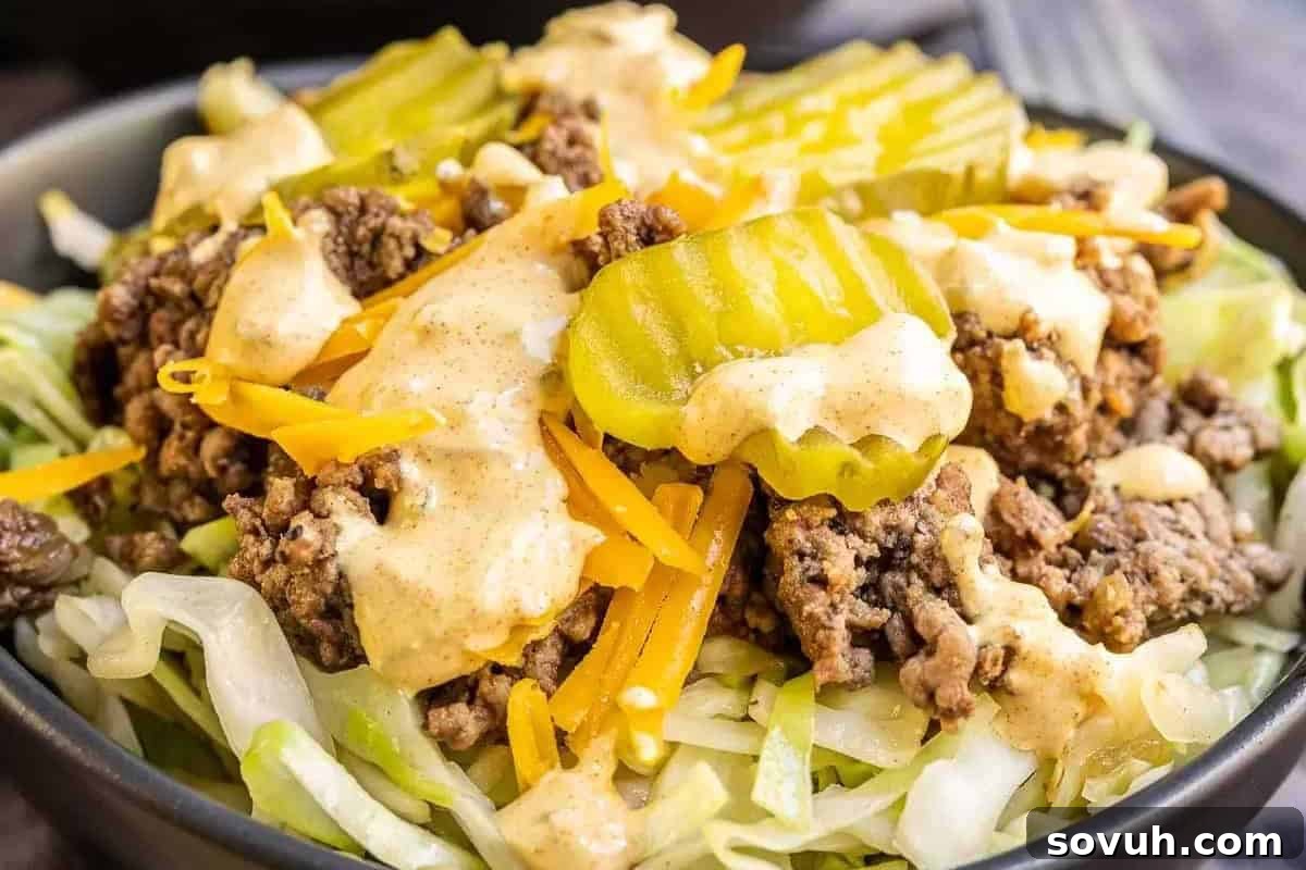 A delightful close-up of a vibrant salad bowl, brimming with seasoned ground beef, generous shredded cheese, tangy pickle slices, and a creamy dressing, all resting on a fresh bed of shredded lettuce.