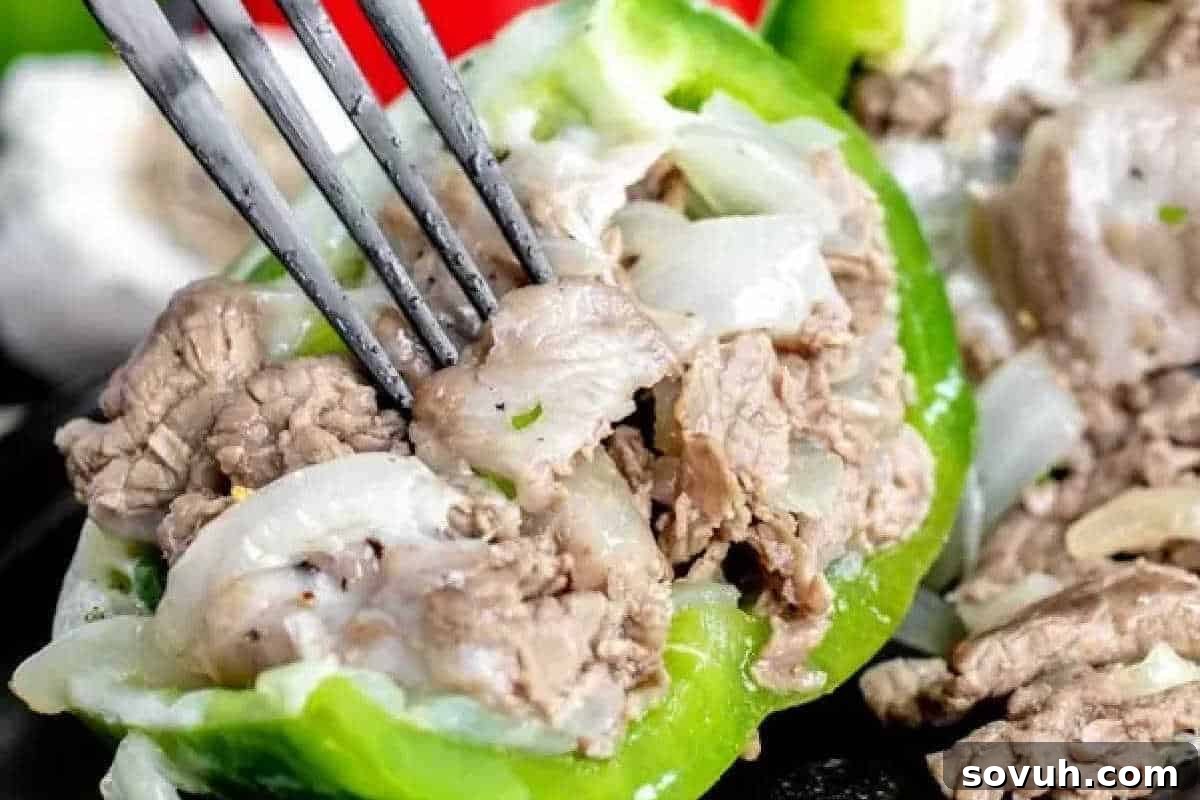 A fork digging into a vibrant green bell pepper generously stuffed with thinly sliced beef, caramelized onions, and melted provolone cheese.