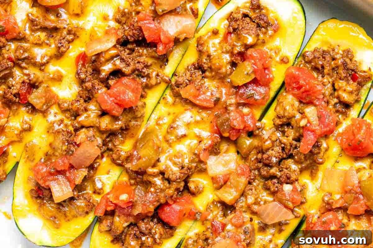 Beautifully prepared zucchini boats, expertly hollowed out and filled with seasoned ground meat, generously topped with melted cheese, vibrant diced tomatoes, onions, and bell peppers.