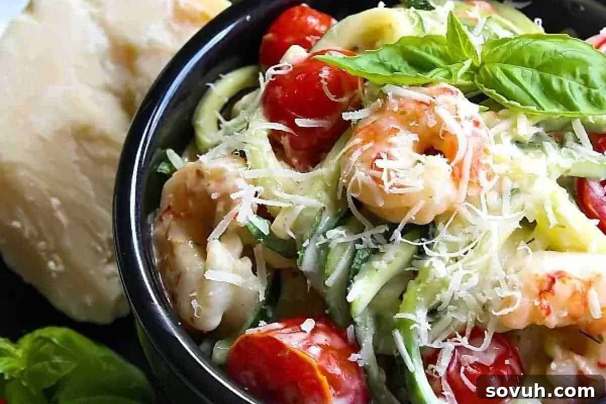 A tantalizing bowl of shrimp and zucchini noodles adorned with bright cherry tomatoes, garnished with grated Parmesan cheese and fresh basil leaves. A block of Parmesan cheese rests in the soft-focused background.