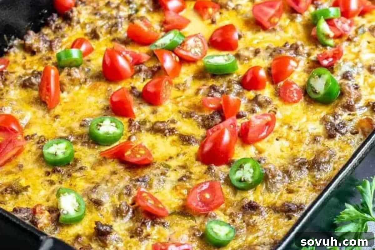 A bubbling casserole generously topped with melted cheese, seasoned ground meat, diced tomatoes, and vibrant sliced jalapeños, baked to perfection in a rustic baking dish.