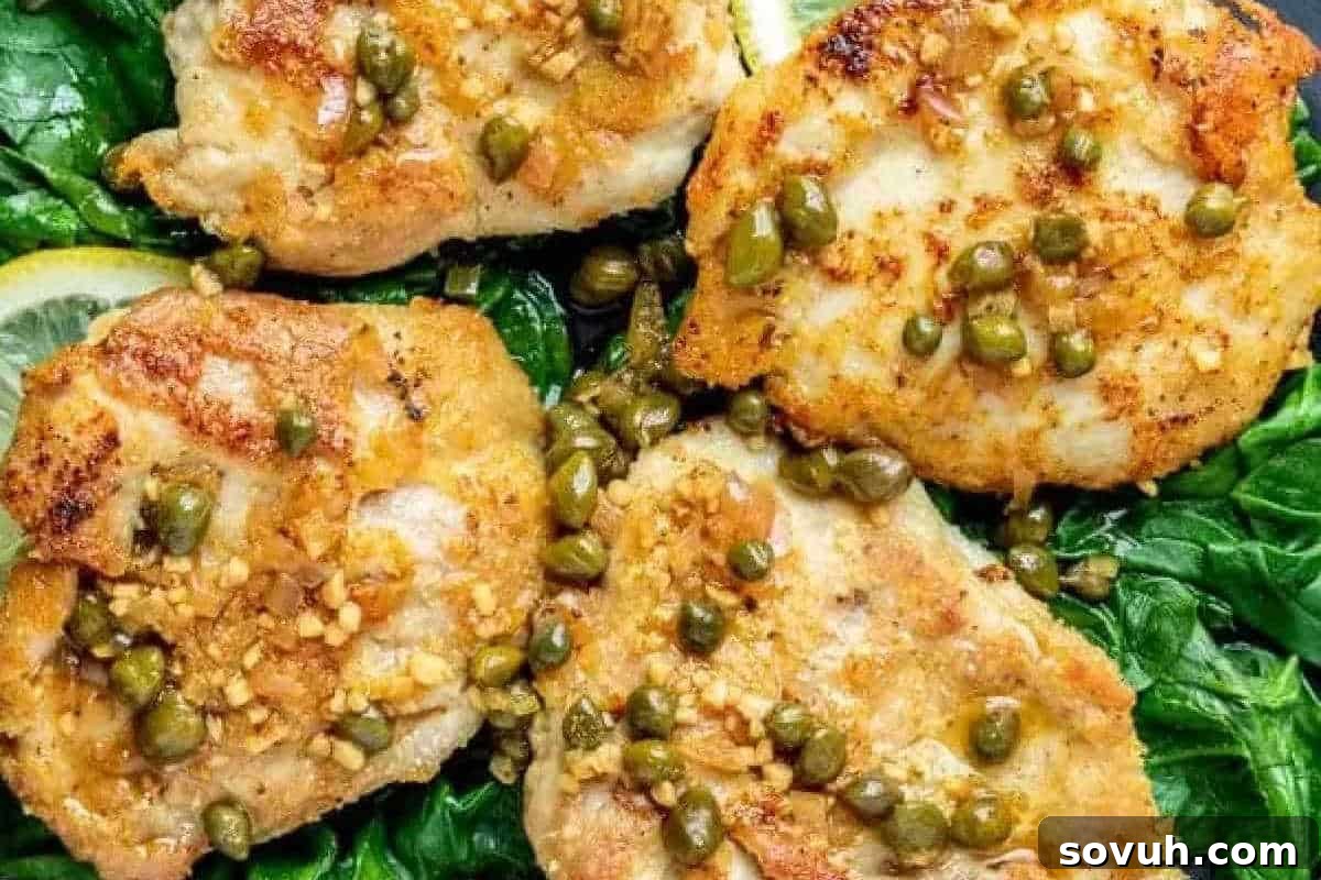 Golden pan-seared chicken breasts, delicately topped with briny capers and aromatic garlic, elegantly served on a bed of vibrant sautéed spinach.