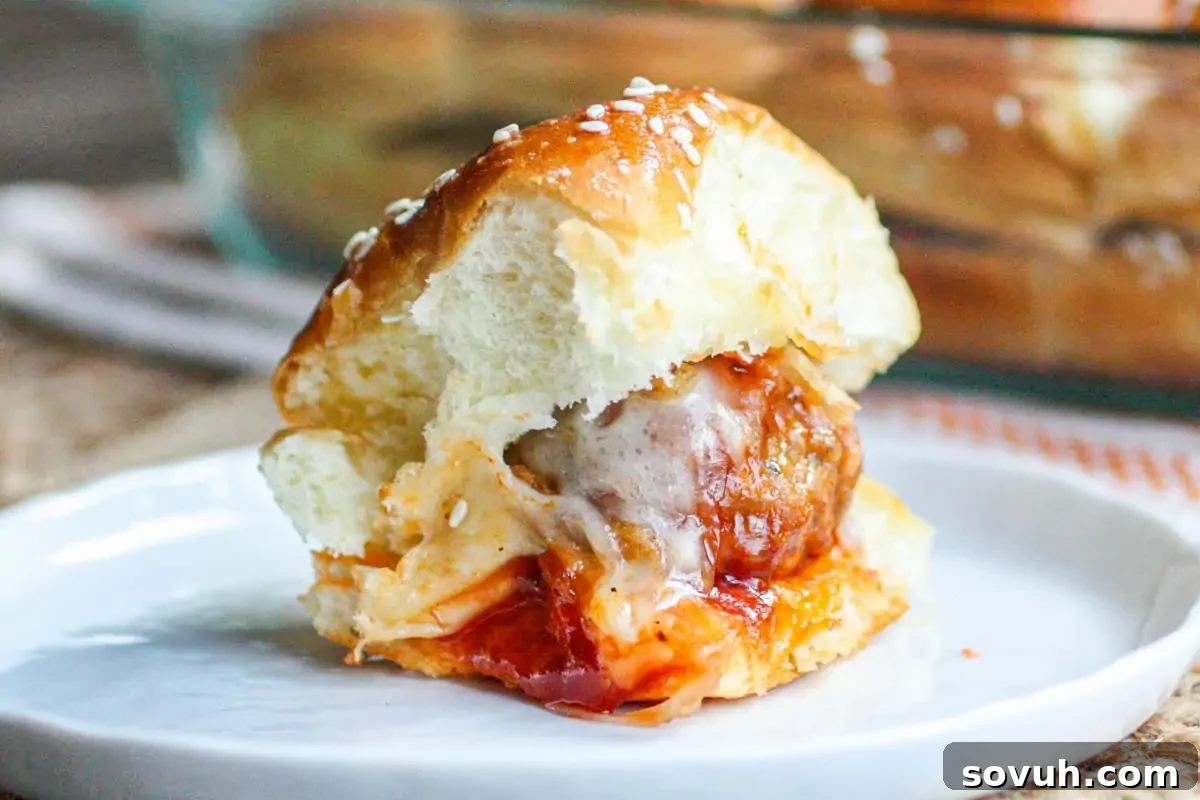A meatball sandwich with marinara sauce and melted cheese in a soft bun, served on a white plate.