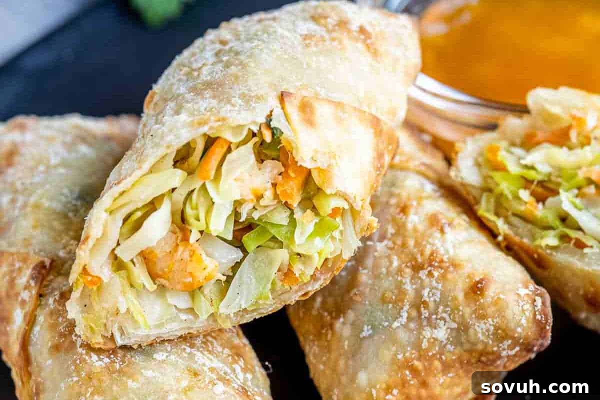 Close-up of several egg rolls filled with shredded vegetables. One is broken open to display the contents. A small glass dish with dipping sauce is in the background.