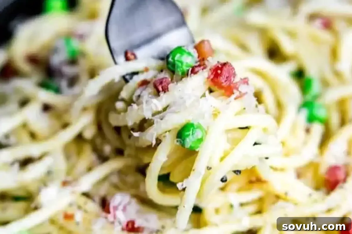 Fork twirls creamy spaghetti with peas, pancetta, and grated cheese, showcasing a classic Italian comfort food.