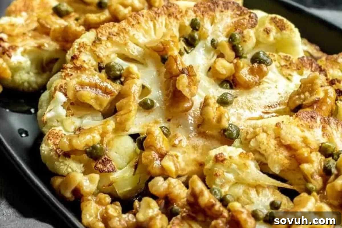 Close-up of roasted cauliflower slices topped with walnuts and capers on a black plate, offering a unique and flavorful vegetable dish.
