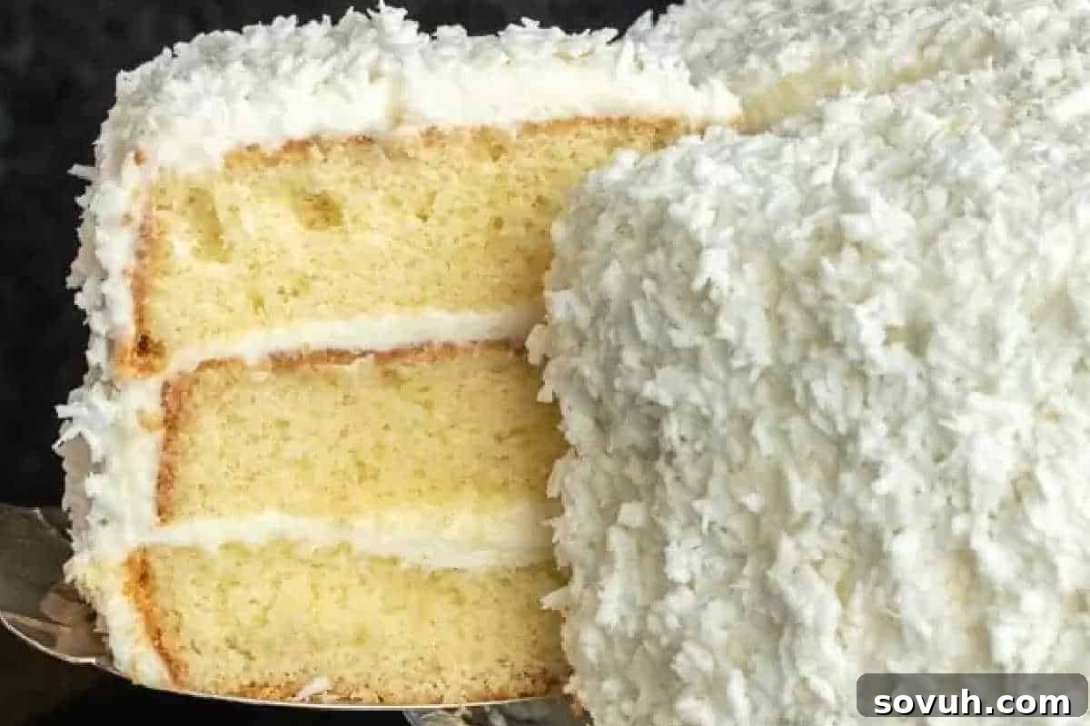 A three-layer coconut cake with white frosting, topped with shredded coconut, showcasing a classic and inviting dessert.