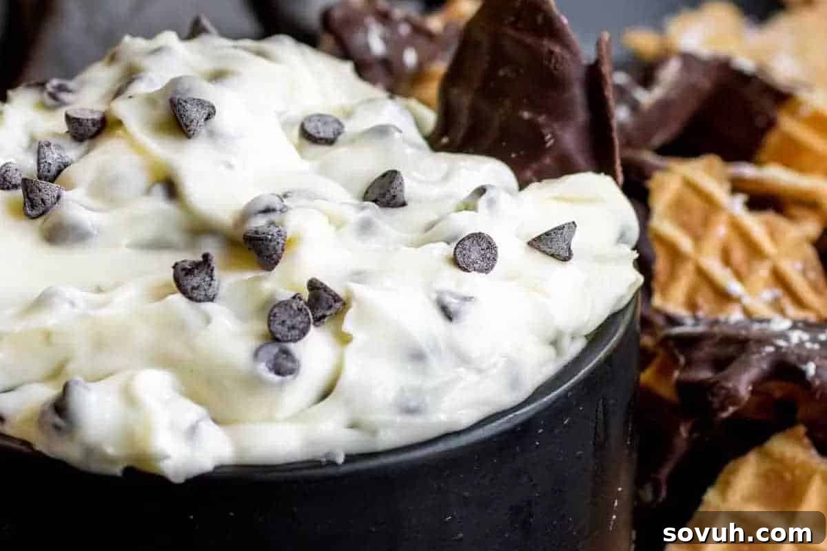 A black bowl filled with creamy white chocolate chip dip. Chocolate-dipped waffle pieces are visible in the background, suggesting a fun, shareable dessert.