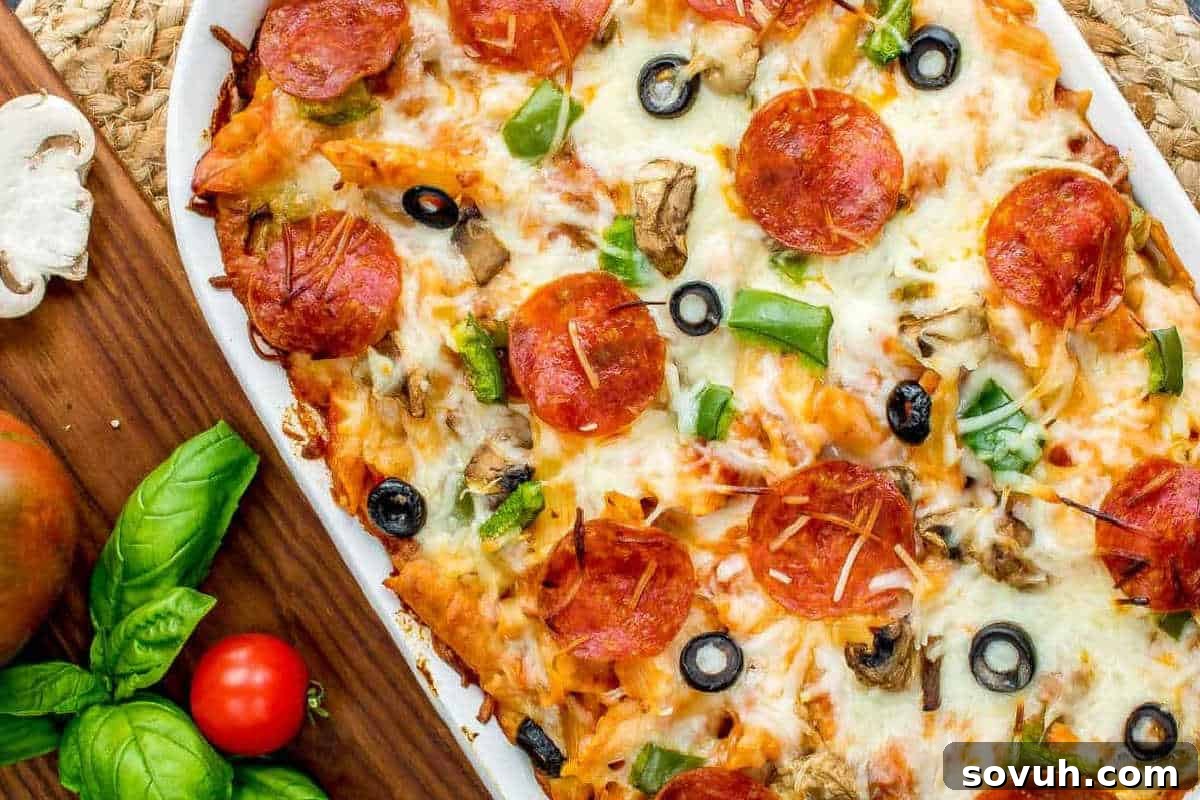 A vibrant pizza casserole, featuring layers of pasta, rich tomato sauce, melted mozzarella cheese, pepperoni, black olives, green bell peppers, and mushrooms, served on a rectangular plate with fresh basil garnish on a wooden surface.