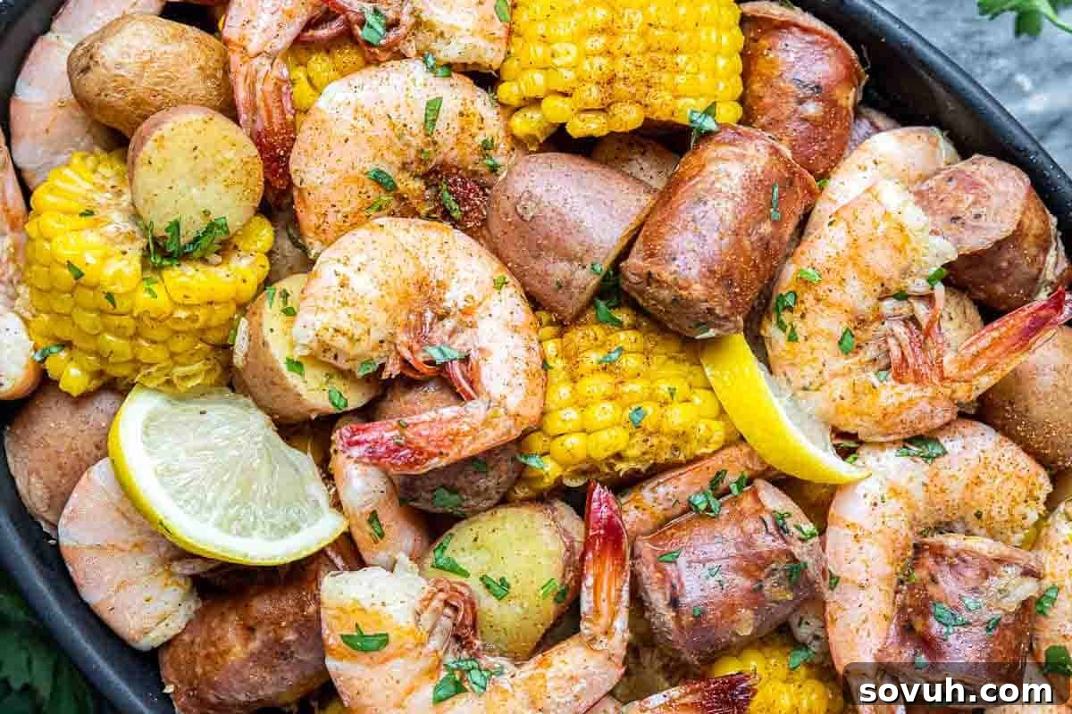 A platter of shrimp, sausage, corn on the cob, potatoes, and lemon wedges, garnished with herbs.