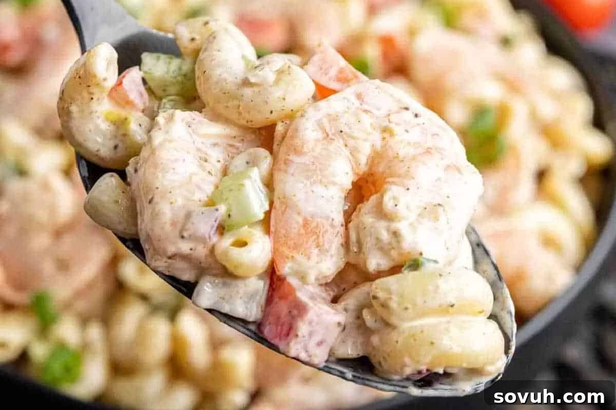 Close-up of a spoonful of creamy macaroni salad with shrimp, diced red bell peppers, and celery.