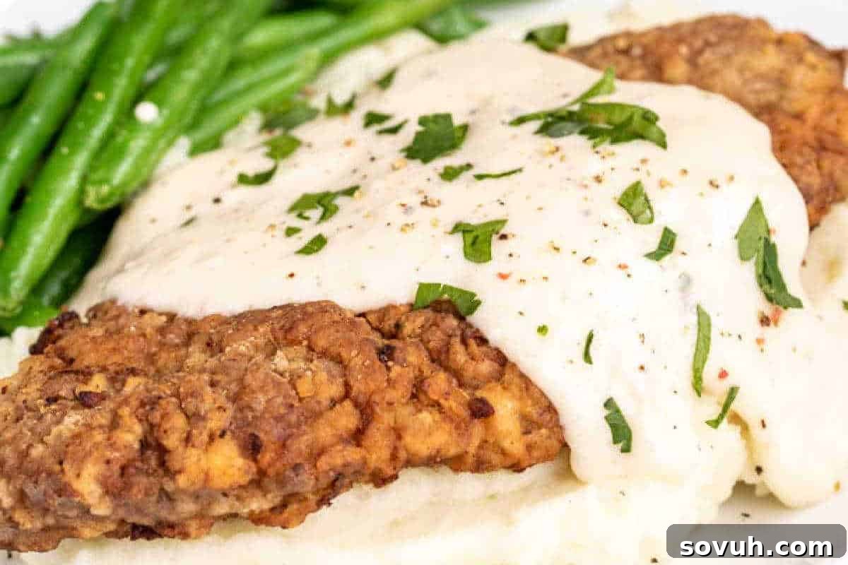 Breaded meat topped with white gravy and herbs, served with mashed potatoes and green beans.