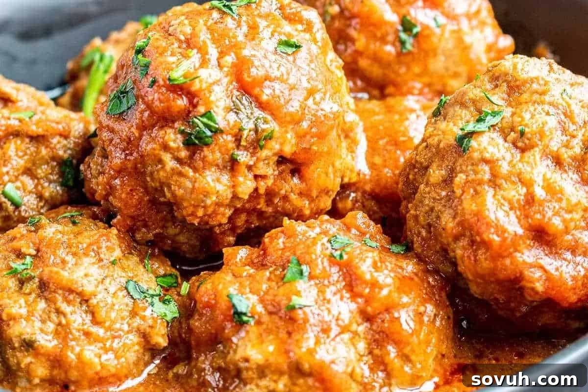 Close-up of several meatballs in a rich tomato sauce, garnished with chopped herbs.