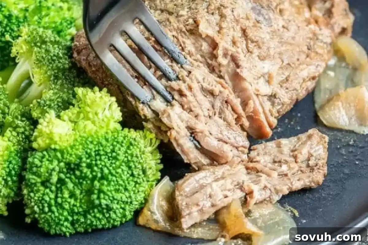 Close-up of a plate with a fork pulling apart cooked meat next to steamed broccoli and onions.