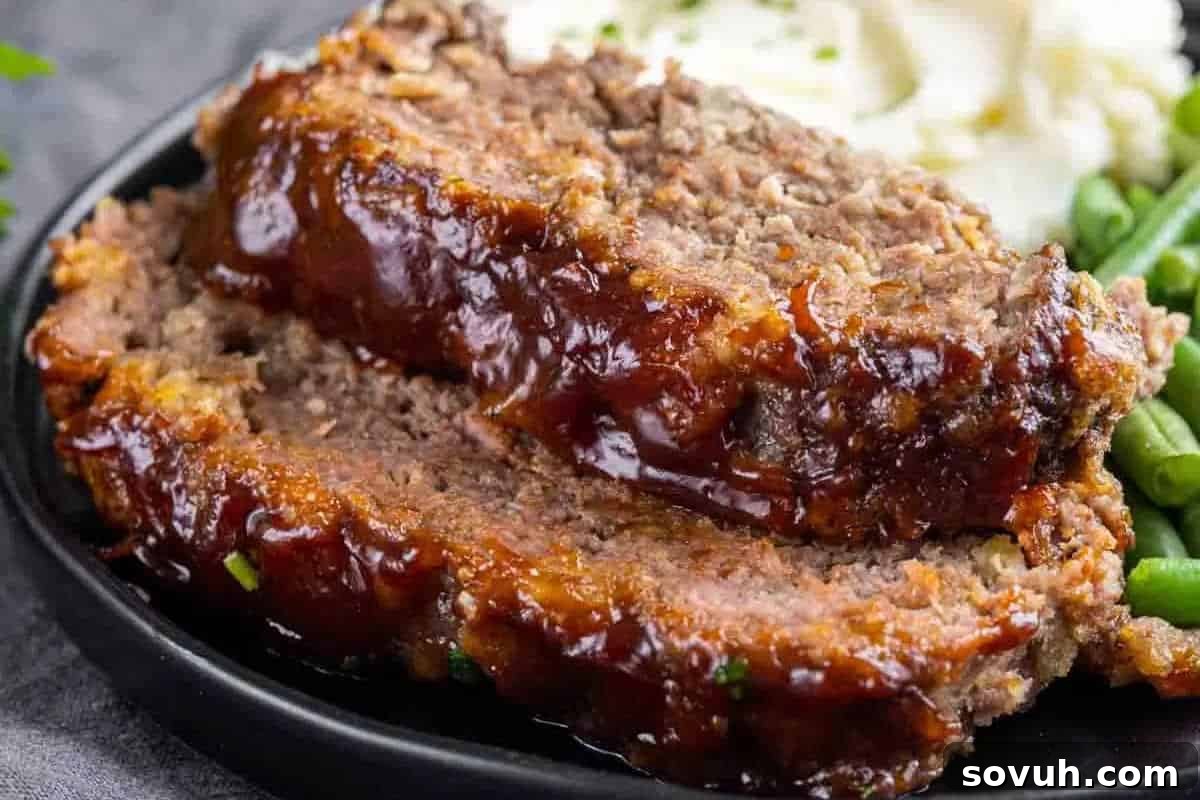 Two slices of glazed meatloaf on a plate, accompanied by mashed potatoes and green beans.