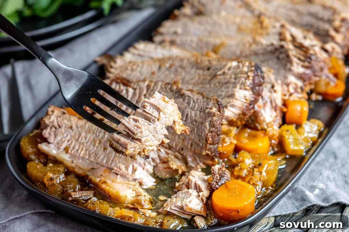 Sliced roast beef with carrots and onions on a dark platter, a fork holding a piece.