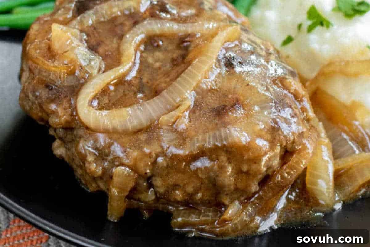 A dish with Salisbury steak, covered in onion gravy, served with mashed potatoes and a side of green beans.