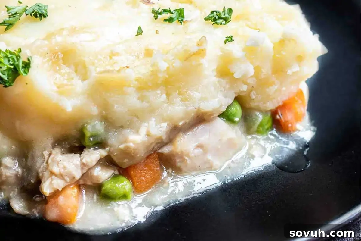 Close-up of a chicken pot pie served on a black plate, featuring mashed potatoes on top, with visible peas, carrots, and chicken pieces.
