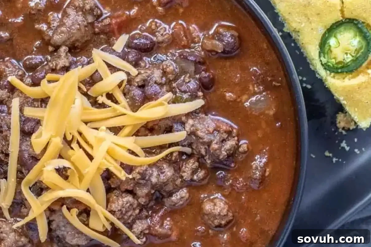 Bowl of chili topped with shredded cheese, served alongside cornbread with a jalapeño slice.