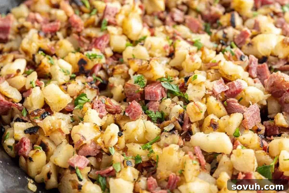 A close-up view of a hearty breakfast skillet, showcasing perfectly diced potatoes, savory corned beef, and caramelized onions, all garnished with fresh parsley.