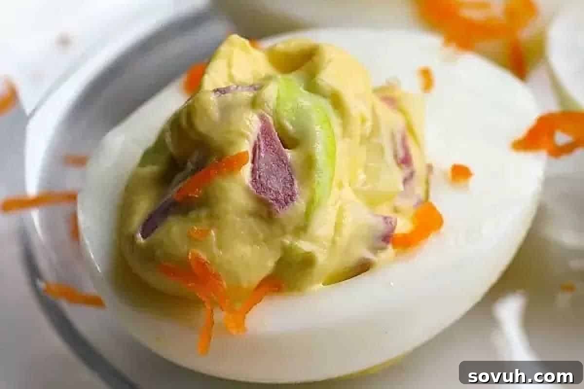 An elegantly prepared deviled egg, topped with a vibrant, creamy filling and artistically garnished with delicate shreds of carrot and finely chopped purple onion.