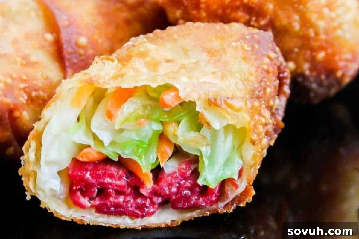 A close-up of a golden-brown, crispy egg roll, sliced in half to reveal a colorful and savory filling of shredded vegetables and tender corned beef.