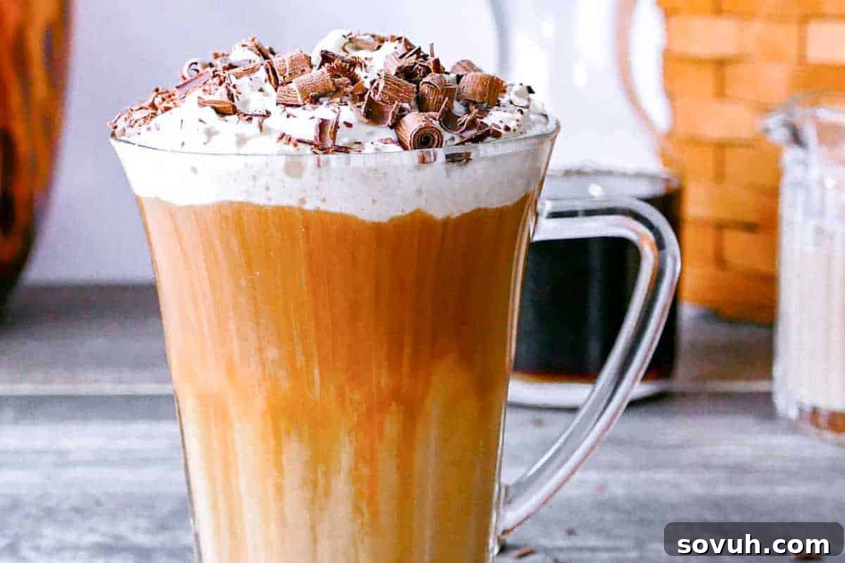 An inviting glass mug filled with frothy latte, elegantly crowned with a generous swirl of whipped cream and delicate chocolate shavings, artfully placed on a natural wooden surface.