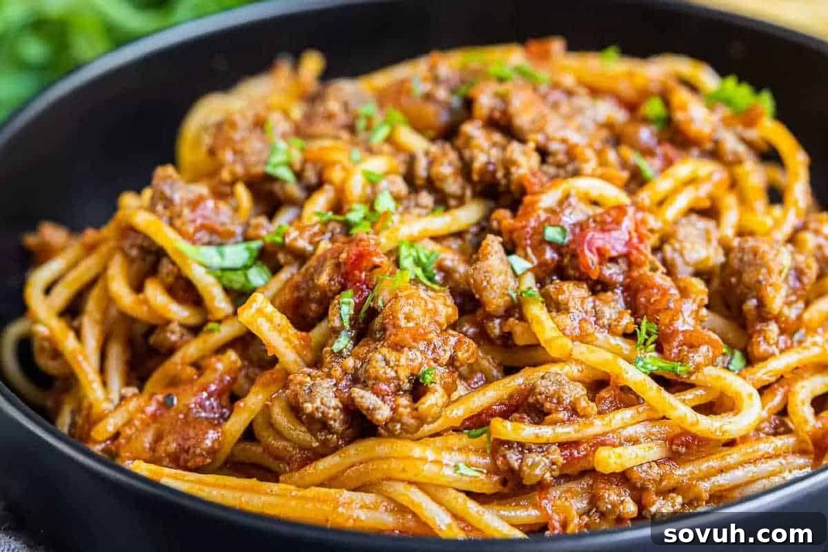 A bowl of spaghetti with meat sauce, garnished with chopped parsley.