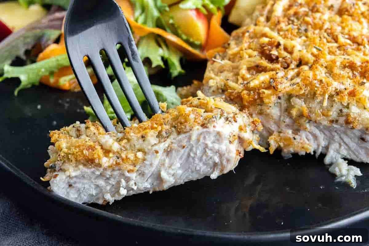 A fork holds a slice of breaded chicken breast on a plate with mixed salad greens in the background.