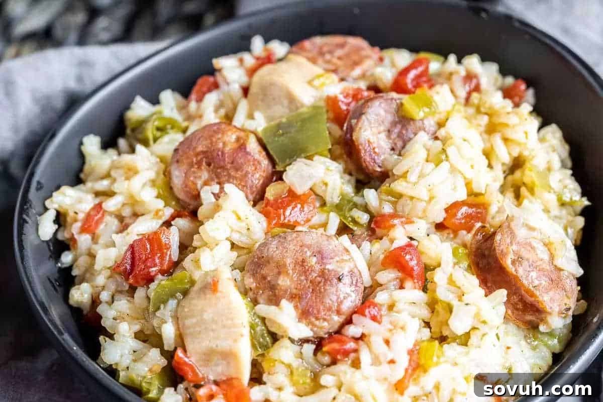 A bowl of rice mixed with sliced sausage, diced bell peppers, tomatoes, and chicken pieces.