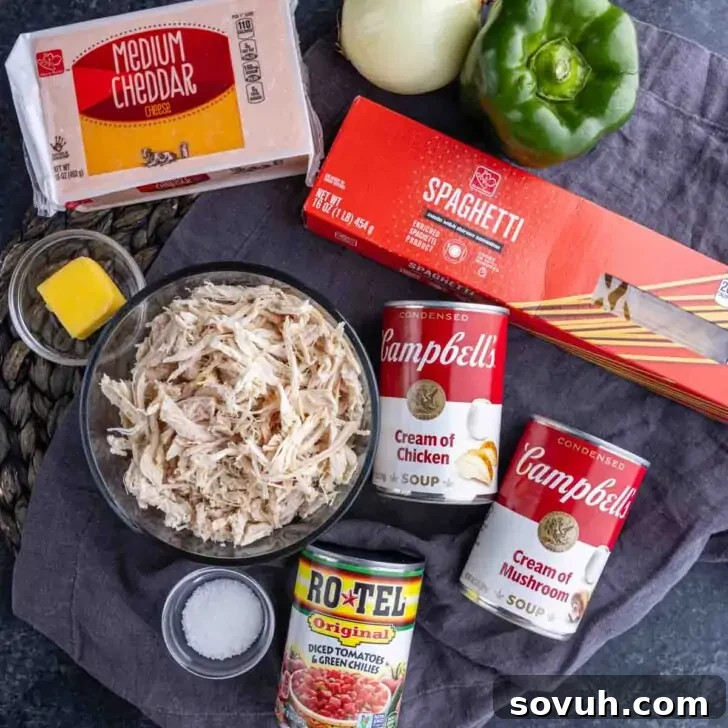 Ingredients on a table: shredded chicken, cream of chicken soup, cream of mushroom soup, cheddar cheese, spaghetti, green pepper, onion, Rotel diced tomatoes, butter, salt.