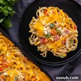 Plate of cheesy spaghetti with mixed vegetables. Another portion is on a tray beside it. Fork and parsley garnish nearby.