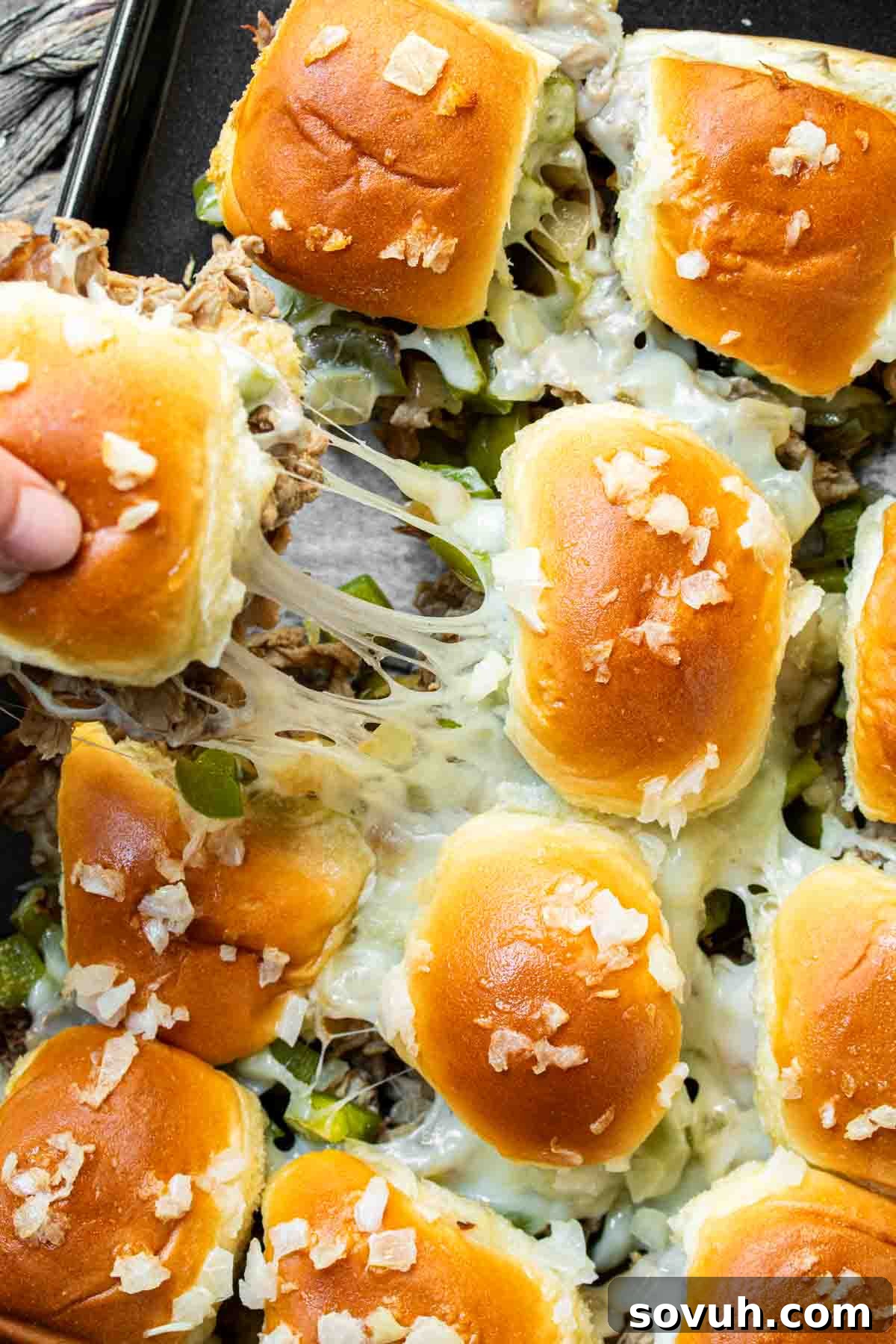 A person reaching for a Philly Cheesesteak Slider from a large tray, emphasizing their shareability.