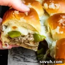 A person is holding two freshly baked Philly Cheesesteak Sliders, showcasing the melted cheese and filling.