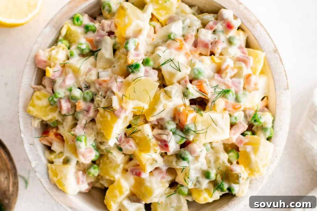 A beautifully arranged bowl of classic Olivier Salad, brimming with perfectly diced boiled potatoes, carrots, and vibrant green peas, all coated in a rich, creamy mayonnaise dressing and elegantly garnished with fresh dill.