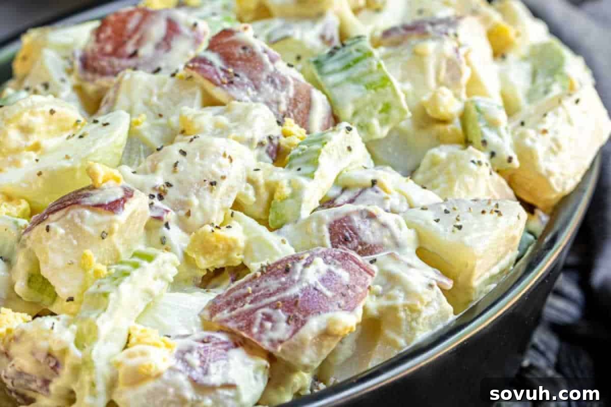 A vibrant bowl of Mustard Potato Salad, showcasing diced red potatoes, crisp celery, perfectly hard-boiled eggs, and a creamy, zesty dressing, garnished with freshly ground black pepper.