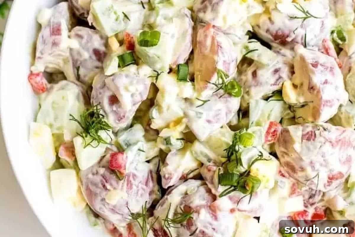A generous bowl of creamy Sour Cream Potato Salad featuring red-skinned potatoes, chopped green onions, finely diced vegetables, and fresh dill, all coated in a rich, white dressing.