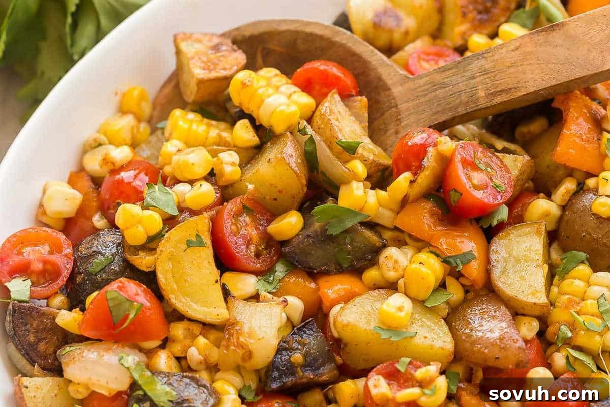 A colorful and vibrant bowl of Southwest Potato Salad, brimming with roasted potatoes, bell peppers, sweet corn kernels, and juicy cherry tomatoes, all garnished with fresh cilantro and a wooden spoon ready for serving.