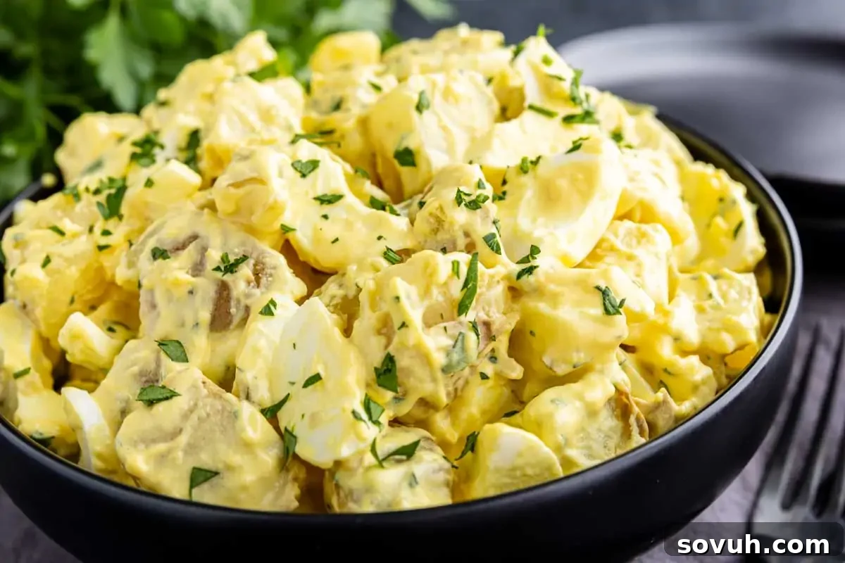 A bowl of creamy potato salad garnished with chopped parsley, placed on a table.