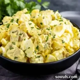 A black bowl filled with creamy potato salad garnished with chopped parsley on a table.