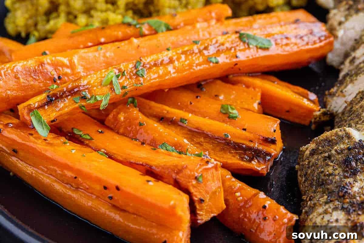 Close-up of roasted carrot sticks garnished with herbs, served on a black plate.